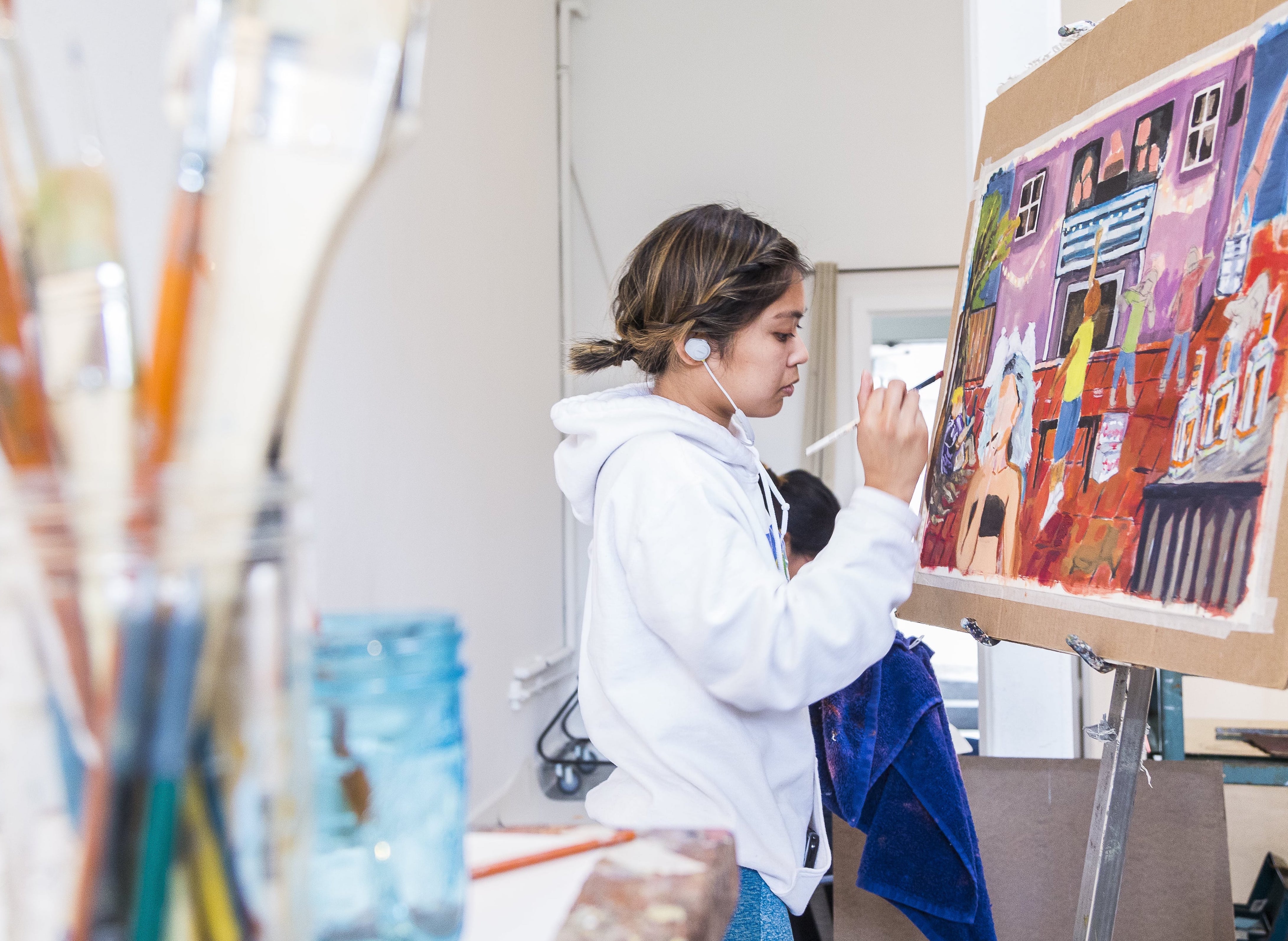 Woman painting on a canvas while being surrounded by art supplies