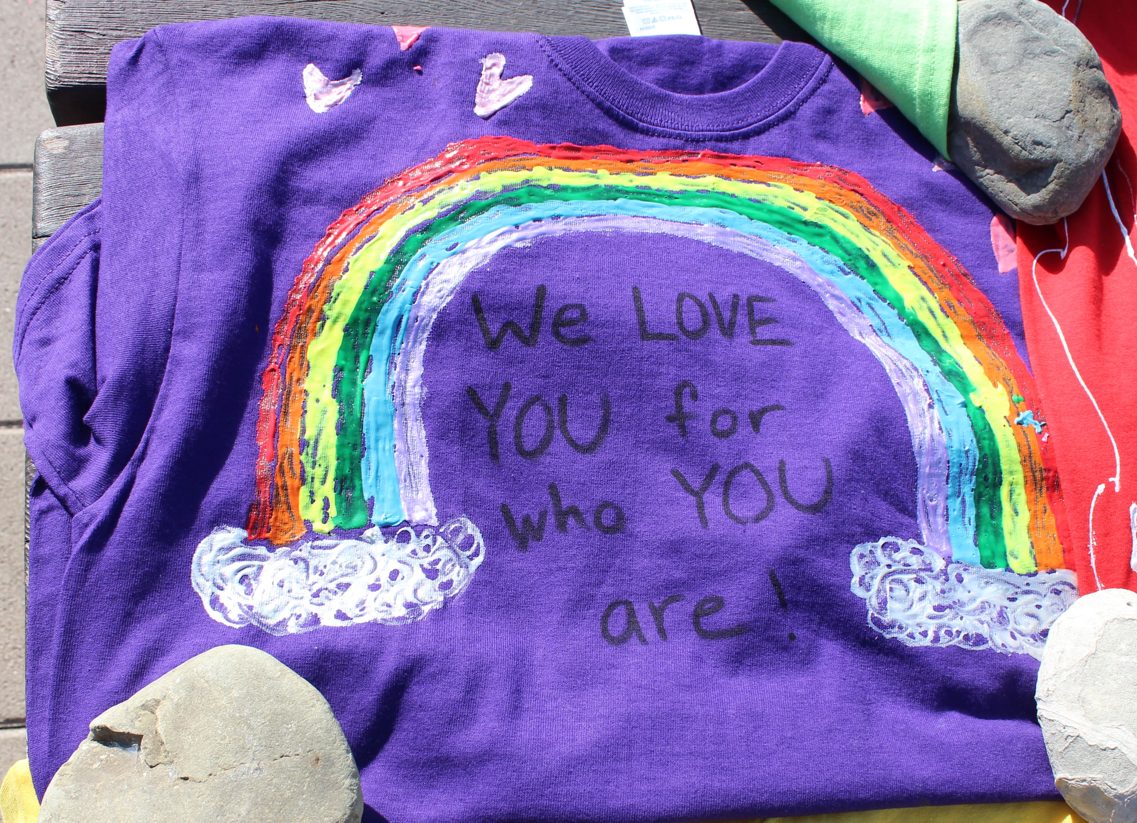 Purple t-shirt with text that says "We Love YOU for who YOU are!" underneath a painted on rainbow