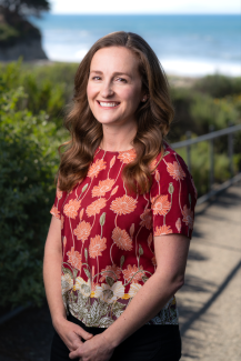 Jamie File Headshot standing in front of greenery and the ocean 