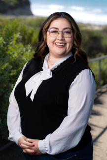 Stephanie Hernandez Carbajal Headshot standing in front of greenery and the ocean 