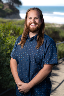 Sven Rundman Headshot standing in front of greenery and the ocean 