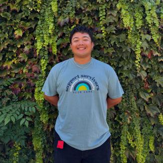 Kaleb standing in front of greenery wearing a blue shirt